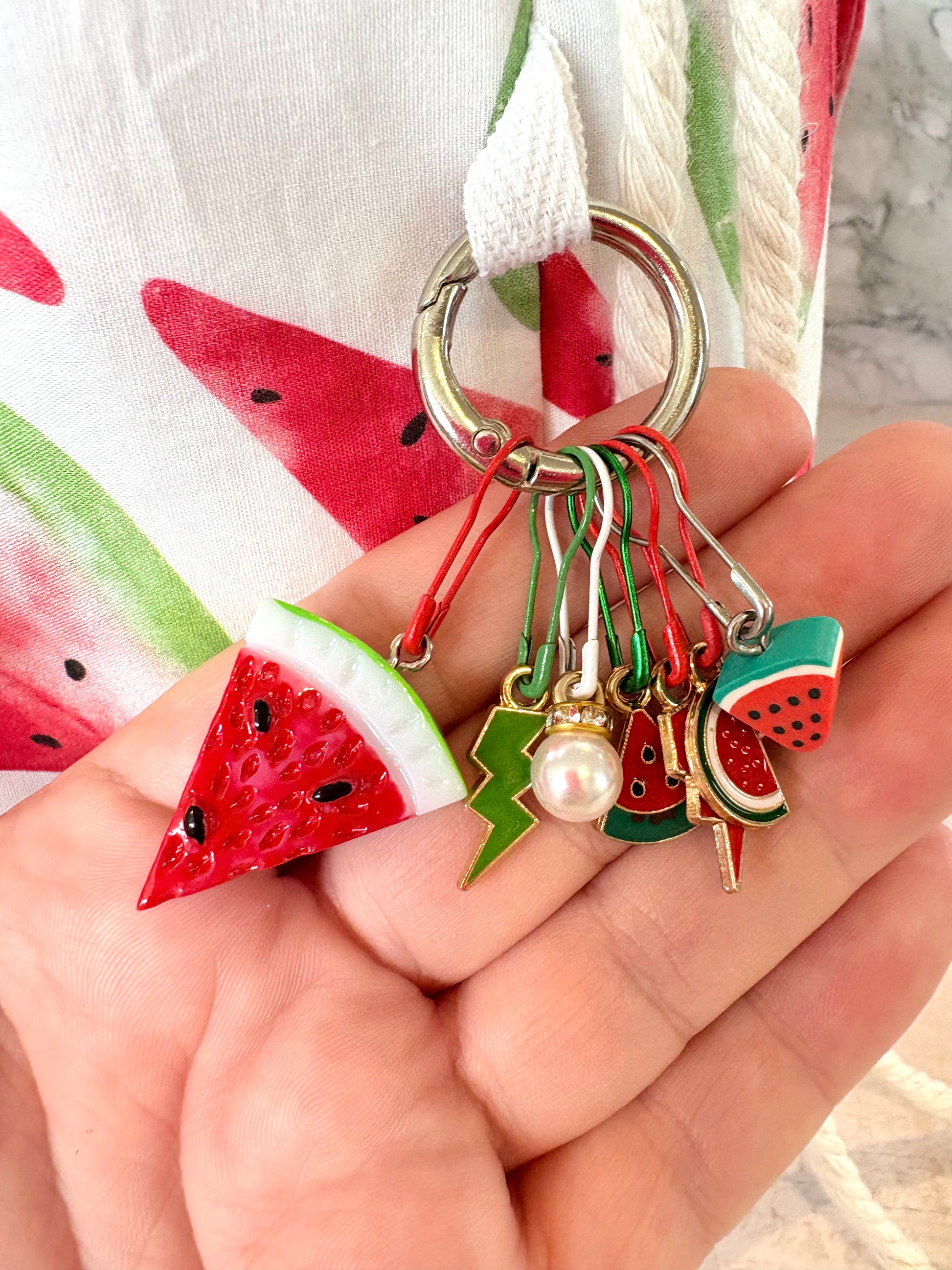 Keychain with watermelon-themed charms held in a hand, with a watermelon-patterned fabric in the background.